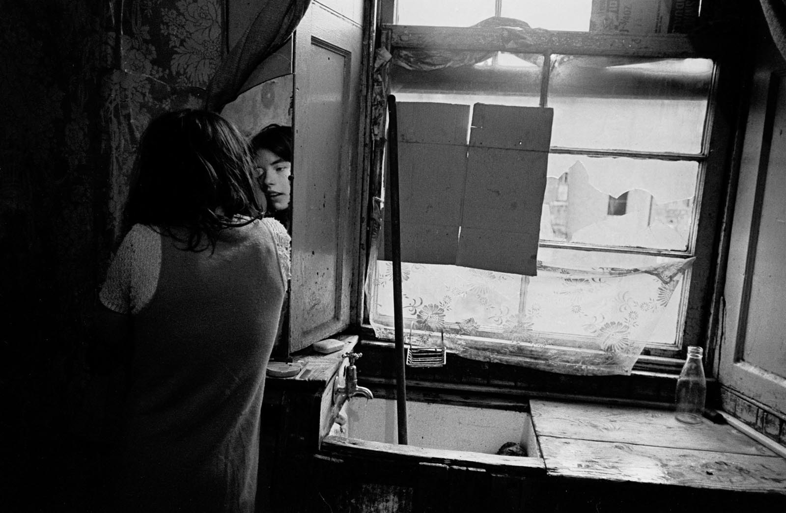 One of the Copeland girls putting on eye makeup in their shattered basement flat. Glasgow, 1970